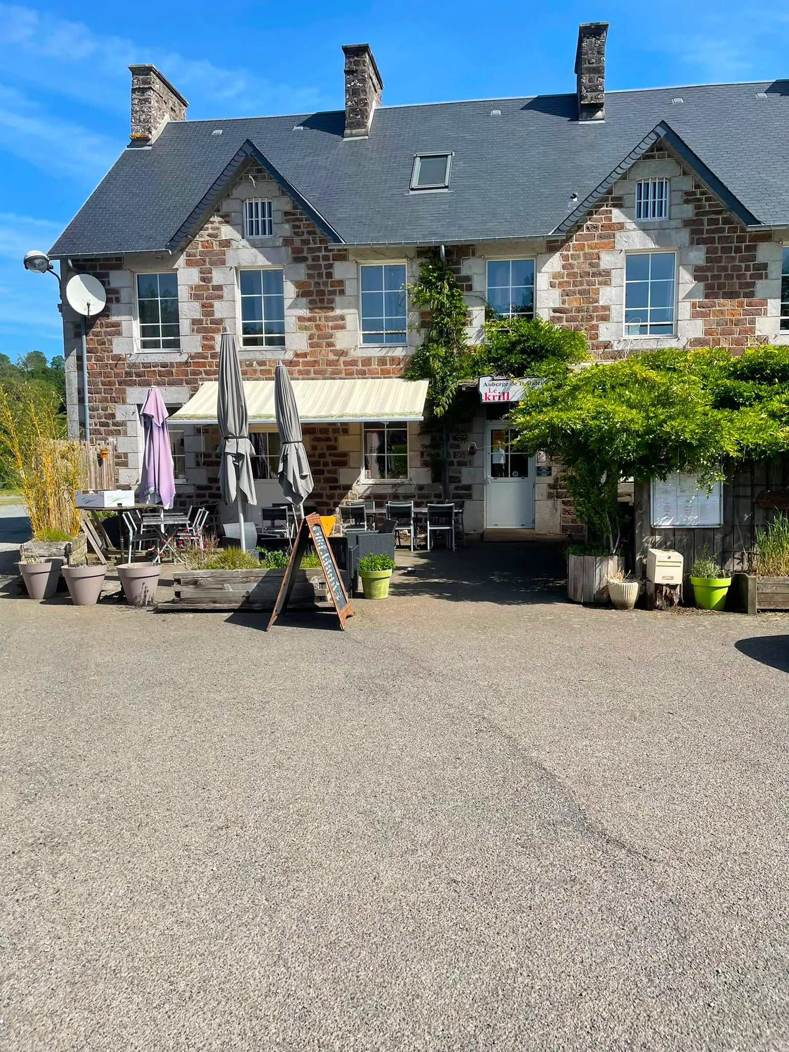 La façade en pierre du restaurant Le Krill à La Baleine, avec sa terrasse et ses parasols